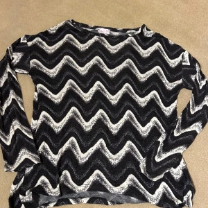 Svartvit mönstrad tröja från Skill - Säljer en cool svartvit tröja från Skill med ett vågigt mönster. Tröjan är långärmad och perfekt för både vardag och fest. Den är i bra skick och redo för en ny ägare. Passar perfekt till jeans eller kjol!