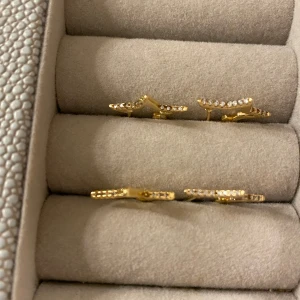 Guldörhängen med stjärndesign - Säljer ett par eleganta guldörhängen med en stjärnformad design. De är i rostfrittstål med guld plätering från ut och Penn! De är dekorerade med små glittrande stenar som ger en lyxig känsla. Perfekta för att lysa upp vilken outfit som helst!❤️