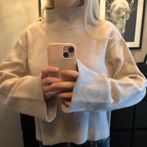 Beige stickad tröja - Säljer en supermysig beige stickad tröja med hög krage. Den har långa ärmar och en loose passform som är perfekt för kyliga dagar. Tröjan är i nyskick och passar perfekt till både jeans och kjol. Perfekt för höst och vinter!
