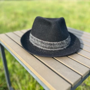 Svart hatt med grått band - Säljer en stilren svart hatt med ett snyggt grått band runtom. Hatten har en klassisk form och är perfekt för både höst och vår. Insidan är fodrad med ett rött tyg som ger en fin kontrast. Köparen  betalar för frakt🚚 