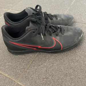 Svarta Nike sneakers med röd detalj - Säljer ett par svarta Nike inomhus skor. De är i bra använt skick och redo för nya äventyr!