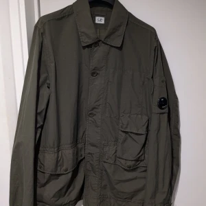 CP Company mörkgrön jacka, storlek 50 - som ny! - En olivgrön jacka från CP-company inköpt i år! Har tyvärr blivit för liten för den så låter den gå vidare.  Jackan har hunnits användas någon gång bara, så den är som ny! Nypriset låg på ca 6000kr   