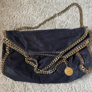 Stella McCartney falabella väska - Stella McCartney väska. Mörkt blå med guldiga kedjor, modellen säljs inte i denna färg längre.  Köpt på Stella McCartneys hemsida Använd men i bra skick.  Pris kan diskuteras vid snabb affär. 