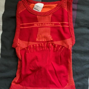 Röd ärmlös topp från Iets Frans - Säljer en  röd ärmlös topp från Iets Frans. Den har ett unikt mönster i orange. Toppen är i syntetmaterial och har en tight passform. Perfekt för dig som vill sticka ut!