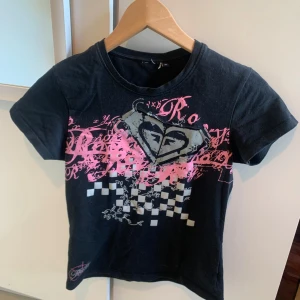 Y2K svart t-shirt med rosa och vitt tryck - Säljer en unik Y2K vintage Roxy t-shirt med ett coolt tryck i rosa och vitt. Perfekt för en avslappnad stil eller en dag ute med vänner! Älskar den så mycket men säljer då den då den inte kommer till användning i min garderob🥰