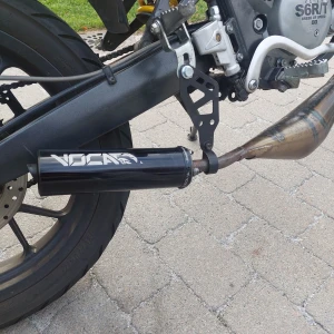 Voca Racing avgasrör för motorcykel - Säljer ett Voca Racing avgasrör som är i bra skick. Det är designat för att ge din motorcykel ett sportigt utseende och förbättrad prestanda. Rören har en snygg svart finish med Voca-loggan i vitt. Perfekt för dig som vill ha en cool look och bättre ljud på din hoj!