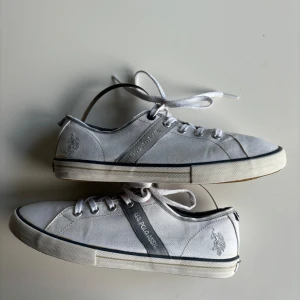 Vita sneakers från U.S. Polo Assn. - Säljer ett par vita sneakers från U.S. Polo Assn. De har en klassisk design med snörning och en diskret logga på sidan. Skorna är i bra skick med en gummisula som ger bra grepp. Perfekta för vardagsbruk och passar till det mesta i garderoben.