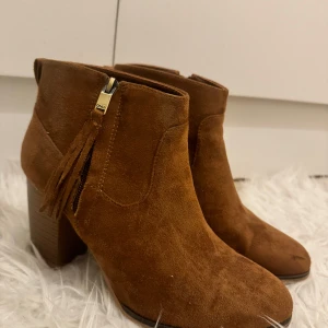 Bruna mocka stövletter med fransdetalj - Säljer ett par snygga bruna stövletter i mocka med en cool fransdetalj vid dragkedjan. De har en bekväm klack och är perfekta för höst och vinter. Passar både till vardags och fest! Använda endast en gång annars som nya! 🌻