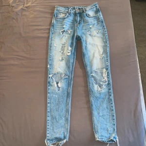 Blå slitna jeans - Säljer ett par otroligt snygga blå jeans från never denim i storlek XS. De har en cool sliten look med flera revor och slitningar på framsidan. Har sytt dit en tygbit under rumpan (inget som syns utifrån). Använda men i bra skick. 
