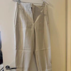 Beige byxor från Zara - Säljer ett par stilrena beige byxor från Zara. De är högmidjade med en rak passform och har diskreta fickor framtill. Perfekta för både vardag och fest!