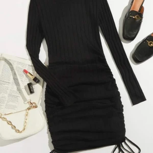 Svart ribbad klänning - Snygg svart ribbad klänning med långärmad design och åtsittande passform. Perfekt för en stilren look. Klänningen har en knytning i nederkant som ger en extra touch. Passar utmärkt för höst och vinter.