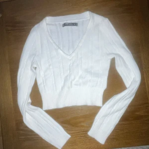 Vit ribbad tröja - Säljer en stilren vit ribbad tröja. Tröjan har en v-ringad design och är croppad med långa ärmar. Perfekt för en trendig look!