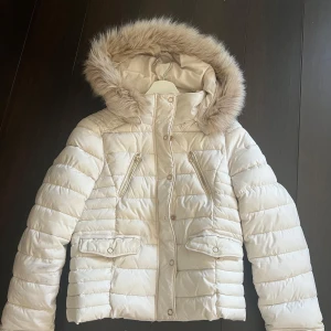 Beige dunjacka från Zara - Säljer en snygg beige dunjacka från Zara som inte finns längre med pälshuva. Jackan har dragkedja och knappar framtill samt praktiska fickor. Perfekt för kyliga och snygga dagar!