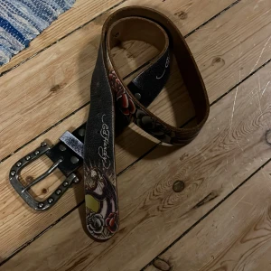 Ed Hardy bälte  - Såååå coolt ed Hardy bälte med en panter och stort spänne. Vet inte storlek men passar nog de flesta. Bra skick med ändats lite mattning i fägen. Må detta komma till ett bra hem hos en cool person. 