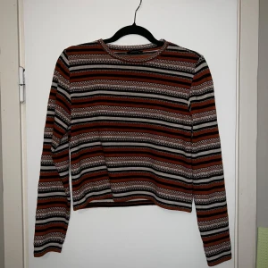 Randig tröja från Monki - Säljer en randig tröja från Monki i svart, orange och vitt. Tröjan har långa ärmar och en rund halsringning.  