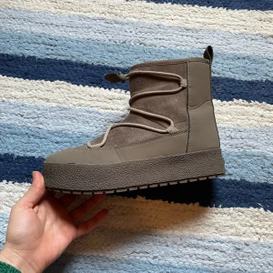 Bruna boots med snörning - Snygga bruna boots med en robust sula och snörning framtill. Skorna har en högre skaft och är perfekta för kyligare väder. Tillverkade i mocka och syntetmaterial för en stilren look. 