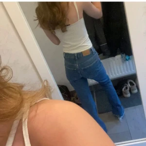 Blå jeans med fransar - Säljer ett par snygga blå jeans med fransiga detaljer vid bensluten. De har en klassisk femficksdesign och en högre midja som ger en bekväm passform. Perfekta för en avslappnad stil. Sliten nere vid foten