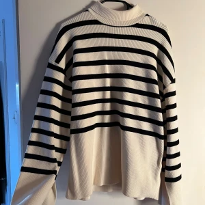 Stickad randig tröja NA-KD - Randig tröja med turtleneck som man kan vika ner, från NA-KD i svart och vit. Tröjan har en ribbad struktur och långa ärmar med en liten slits längst ner på armen. 