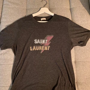 Mörkgrå t-shirt från Saint Laurent - Tjenare, säljer nu min mörkgrå t-shirt från Saint Laurent då jag har växt ur den. Finns inga skador på den och passar perfekt nu till våren/ sommaren 