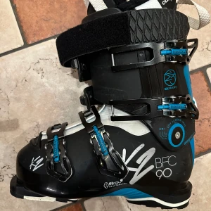 Slalompjäxor, Svarta och blåa pjäxor från K2 - Säljer ett par svarta och blåa pjäxor med vita detaljer från K2 med justerbara spännen och vadderad Chrusfit linear insida. K2 BFC är en pjäxa som kombinerar låg vikt, prestanda och komfort för att göra dagarna i backen så behagliga som möjligt. Läst på 103mm (normala till breda fötter). Powerfuse spyne (spänne baktill på pjäxa för att bli mindre styv när man går,  spänns vid skidåkning).  Även inlägg bak i pjäxa för extra lutning som enkelt kan tas av och på med kardborrfäste. 