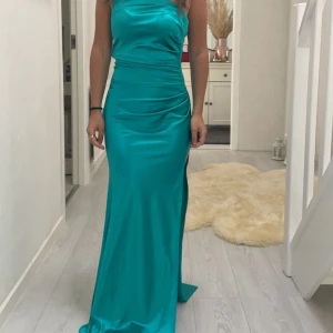 Gyllengrön långklänning i satin - Helt ny, endast testad! Köpte denna och en blå till balen men bestämde mig för den blå. Klänningen har även en slit.