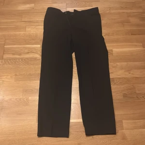 Svarta kostymbyxor från Hugo Boss - Eleganta svarta kostymbyxor från Hugo Boss. Byxorna har en klassisk rak passform och är perfekta för en stilren look. De är tillverkade i ett högkvalitativt material som ger en bekväm känsla hela dagen. Längden på byxorna är 110 cm och midjan är 47 cm.