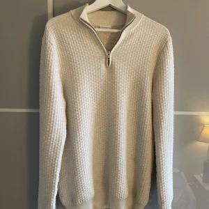 Half zip från John Henric - Säljer en stilren vit stickad tröja från John Henric. Tröjan har en halv dragkedja vid halsen och en texturerad yta som ger en snygg look. Perfekt för kyligare dagar.