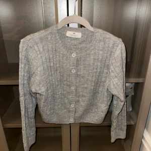 Grå stickad kofta från H&M - Säljer en stilren grå stickad kofta från H&M. Koftan har långa ärmar och knappar framtill, perfekt för kyligare dagar. Enkel och tidlös design som passar till det mesta. Perfekt för lager-på-lager-stilen.