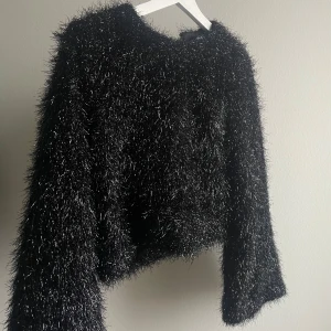 Svart fluffig tröja från Gina Tricot - Säljer en glittrig och fluffig svart tröja från Gina Tricot. Tröjan har en glittrig finish som ger en extra touch av glamour. Den är långärmad och har en normal passform. Använd fåtal gånger! 