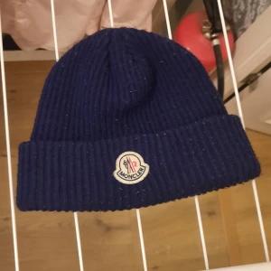 Mörkblå ribbad mössa från Moncler - Snygg mörkblå mössa från Moncler med ribbad design och broderad logga framtill. Perfekt för kyliga dagar och ger en stilren look. Passar bra till både vardag och mer uppklädda tillfällen.