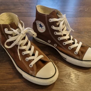 Converse Chuck Taylor All Star Hi Nya - Nya Converse Chuck Taylor All Star Hi. Brun med klassisk vit gummisula och snörning. Skorna har den ikoniska All Star-loggan på sidan och är perfekta för en avslappnad stil. Canvastyg, luftventiler. Storlek: US mens 5,5. US womens 7,5. UK 5,5. EUR 38