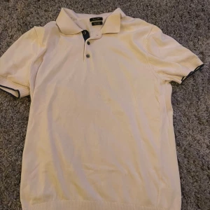 Vit pikétröja från massimo dutti - Säljer en stilren vit pikétröja från massimo dutti med klassisk krage och knappar framtill. Tröjan har korta ärmar med svarta detaljer vid ärmslut och krage. Perfekt för en avslappnad men snygg look.