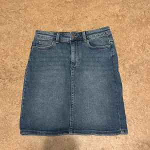 Jeanskjol från Pieces - Snygg jeanskjol från Pieces i klassisk blå denim. Kjolen har en normal passform med femficksdesign och knappstängning fram. Perfekt för en avslappnad stil.