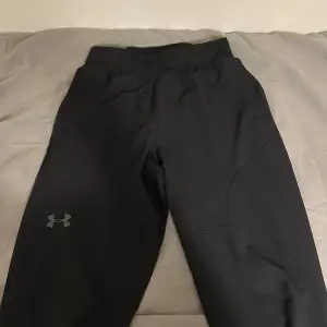 Snygga svarta träningsbyxor från Under Armour med elastisk midja och dragkedja på bakfickan. Perfekta för träning med sin bekväma passform och stilrena design.