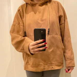 Brun hoodie från Zara - Säljer en mysig brun hoodie från Zara med justerbara snören i huvan. Perfekt för en avslappnad stil. Den har en stor ficka framtill och långa ärmar.