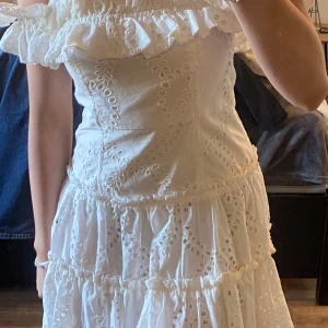 Vit offshoulder klänning med volang / studentklänning  - Charmig vit klänning med offshoulder-design och volangdetaljer. Klänningen har ett vackert broderat mönster och en luftig, romantisk stil. Perfekt för sommarens festligheter. Dragkedja finns på ena sidan!🧸🌸