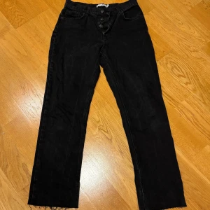 Svarta jeansbyxor - Snygga svarta jeansbyxor med knappar framtill. De har en klassisk femficksdesign och en rak passform som ger en avslappnad look. Perfekta för en stilren vardagsstil.