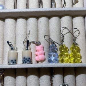 Färgglada örhängen med boba och gummibjörnar - Unika örhängen med boba-te och gummibjörnsdesign. Innehåller ett par med boba-te i glasflaskor och flera par med gummibjörnar i rosa, blått och gult. Perfekt för att lägga till en lekfull touch till din stil.