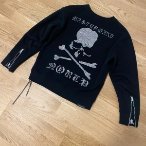 Svart tröja från Mastermind size M - Snygg svart tröja från Mastermind med ikoniskt dödskallemotiv i glittrande stenar på ryggen. Tröjan har långa ärmar med dragkedjor och är tillverkad i 100% bomull. Perfekt för en cool och edgy stil.