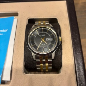 Citizen herrklocka med silver och gulddetaljer - Snygg Citizen herrklocka med en stilren svart urtavla och dag/datumvisning. Kvitto och extra länkar finns.