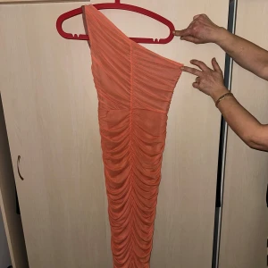 Orange oneshoulder klänning - Snygg orange oneshoulder klänning med rynkade detaljer. Perfekt för en kväll ute eller en speciell tillställning. Klänningen har en smickrande passform.