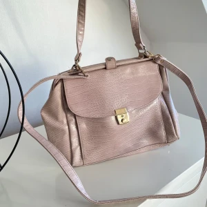 Beige axelväska med krokodilmönster - Snygg beige axelväska i syntetmaterial med krokodilmönster. Väskan har en praktisk axelrem och ett elegant lås framtill. Perfekt för att ge din outfit en stilfull touch.