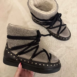 Grå och svarta boots från Inuikii - Säljer min syrras snygga och varma boots från Inuikii i grått och svart med fårskinnsfoder. Skorna har dekorativa nitar och snörning som ger en unik look. Perfekta för kalla dagar.