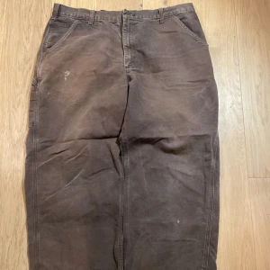 cargobyxor från Carhartt - Säljer ett par bruna cargobyxor från Carhartt  Byxorna har en baggy passform och är perfekta för en street wear stil. Det finns en liten slitagefläck på framsidan (personligen tycker jag att det ger den en vintage look)