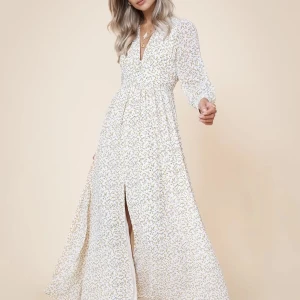 Vit blommig långklänning ADOORE - Elegant vit långklänning med blommigt mönster och v-ringad design. Klänningen har långa ärmar och en stilfull slits framtill, perfekt för en somrig look. Storlek 38. Använd en gång.