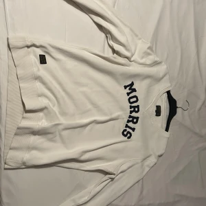 Vit tröja från Morris - Säljer en stilren vit tröja från Morris med mörkblå text på bröstet. Tröjan har långa ärmar och en rund halsringning. Perfekt för en avslappnad look.