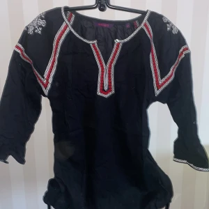 Svart blus med broderi st.S/M - Snygg svart blus med vackra broderade detaljer i vitt och rött. Blusen har trekvartsärmar och en dekorativ v-ringning, på etiketten står det xxl den är S/M. Perfekt för en bohemisk stil.