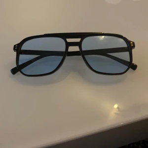 Svarta solglasögon med blå linser - Snygga svarta solglasögon med en klassisk pilotform och blå tonade linser. De har en dubbel brygga och smala skalmar som ger en stilren look. Perfekta för soliga dagar och en cool stil.