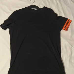 Svart Dsquared t-shirt med orange detalj - Snygg svart t-shirt med en iögonfallande orange detalj på ärmen. Perfekt för en avslappnad stil. (ÄKTA)