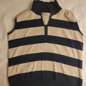 Randig väst från Class International - Snygg ärmlös väst från Class International med breda horisontella ränder i beige och blå. Västen har en dragkedja framtill och är tillverkad i en bomulls- och akrylblandning. Perfekt för en stilren och avslappnad look.